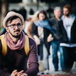 A stylish man in a trendy outfit stands out on a busy city street with various people in the background.